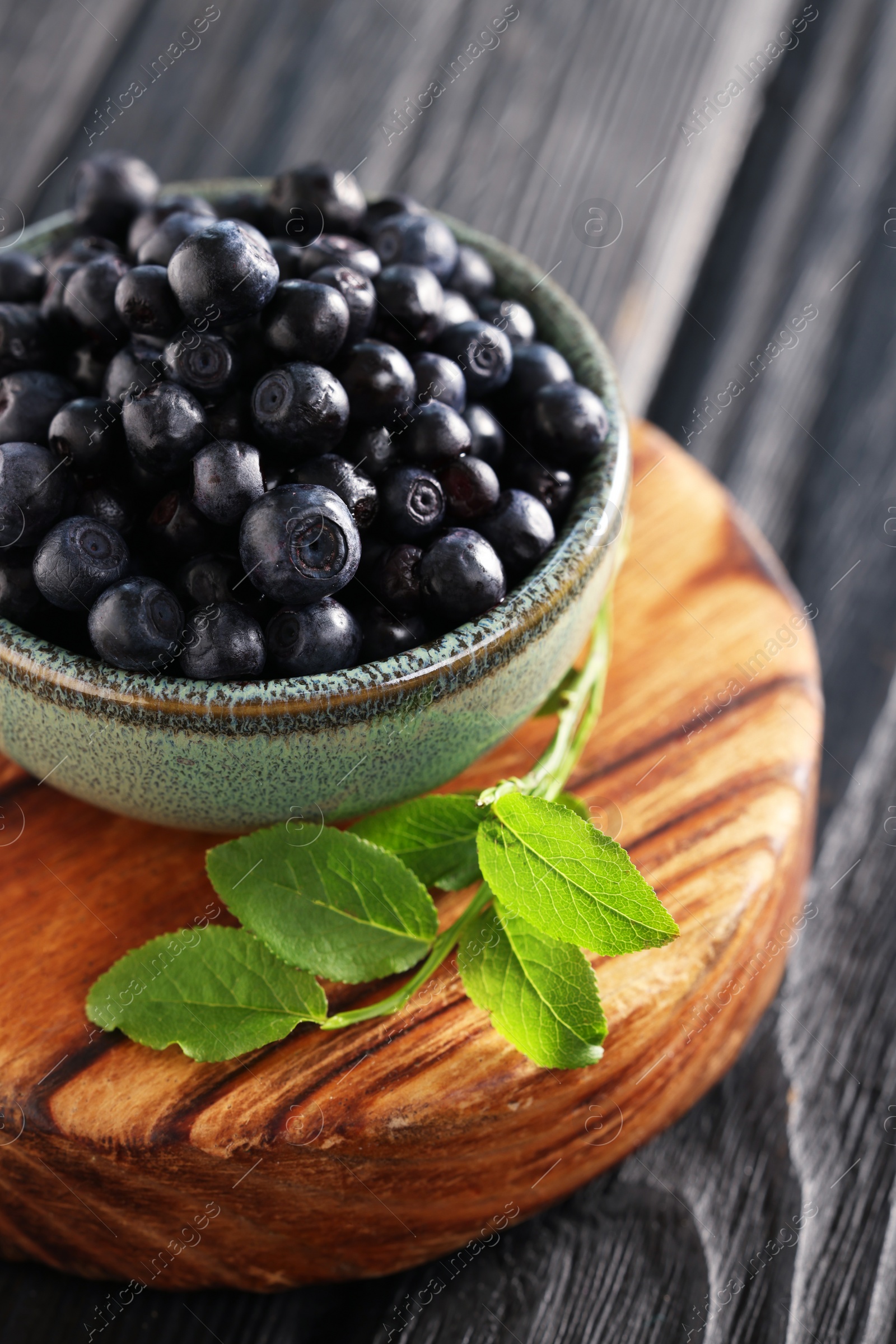 Photo of Bowl of tasty fresh bilberries and green leaves on wooden table, closeup