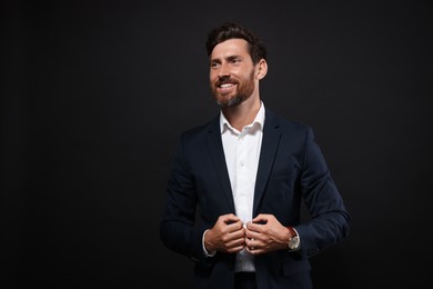 Photo of Portrait of smiling bearded man in suit on black background. Space for text