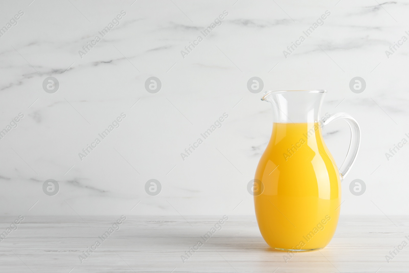 Photo of Fresh orange juice in glass jug on white wooden table, space for text