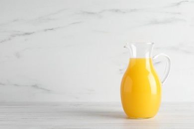 Fresh orange juice in glass jug on white wooden table, space for text