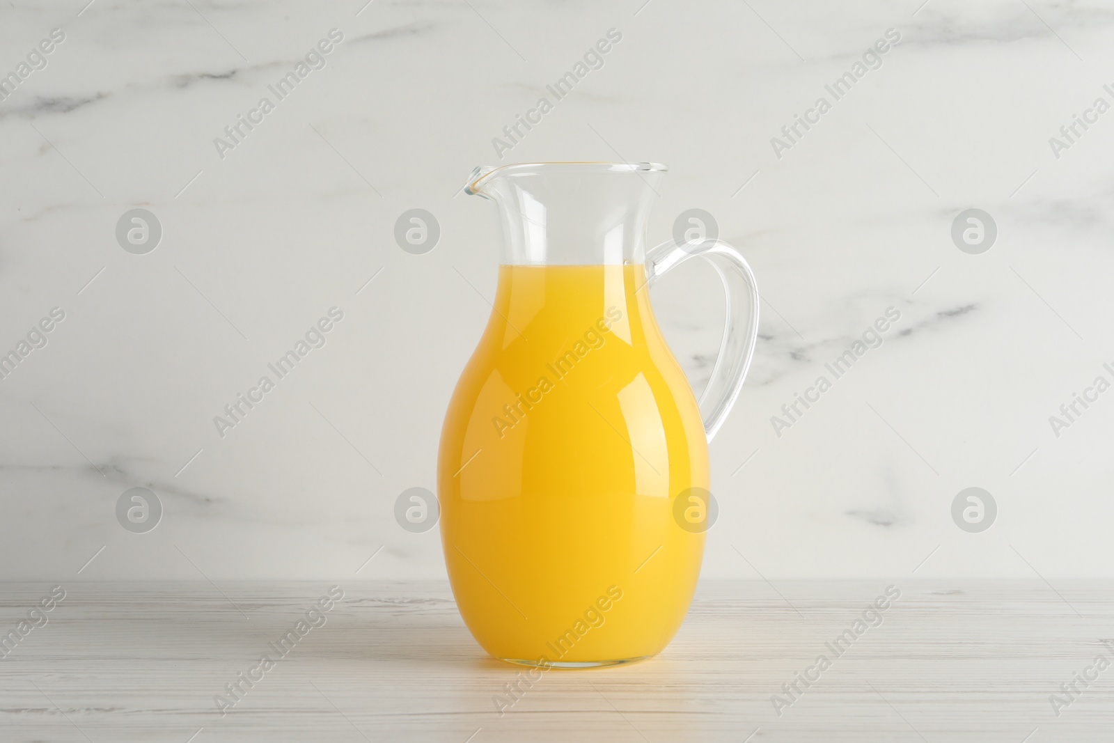 Photo of Fresh orange juice in glass jug on white wooden table