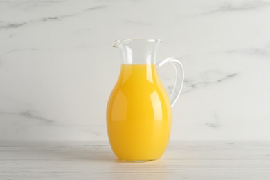 Photo of Fresh orange juice in glass jug on white wooden table