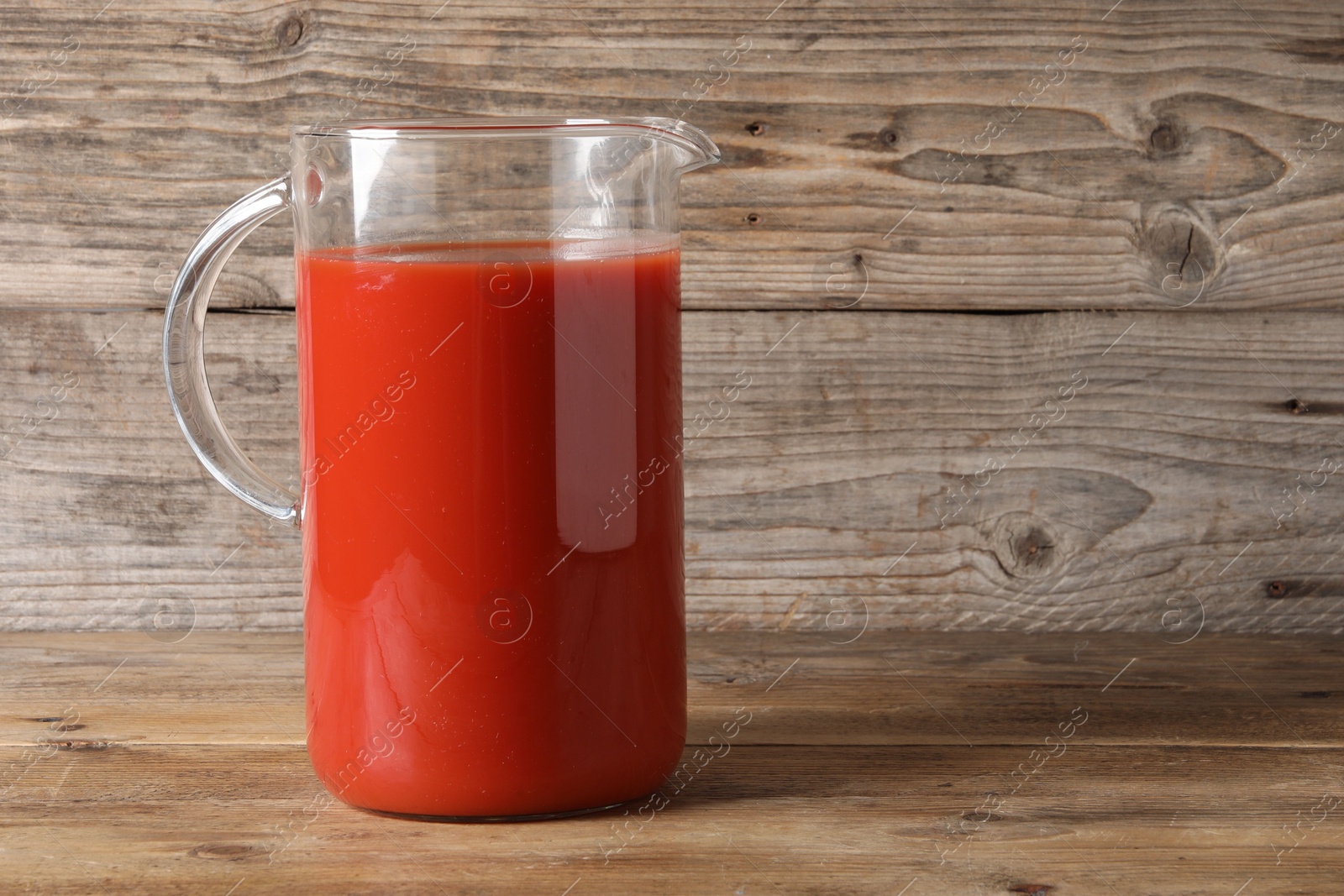 Photo of Fresh tomato juice in glass jug on wooden table, space for text