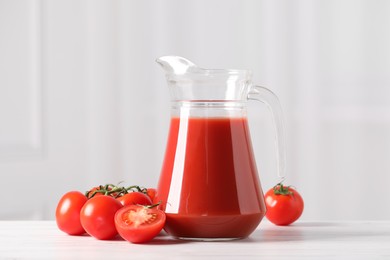 Tasty tomato juice in glass jug and fresh vegetables on white table