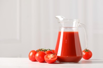 Photo of Tasty tomato juice in glass jug and fresh vegetables on white table. Space for text