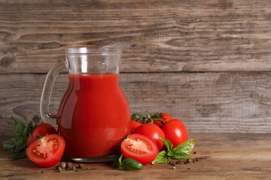 Tasty tomato juice in glass jug, fresh vegetables and spices on wooden table. Space for text