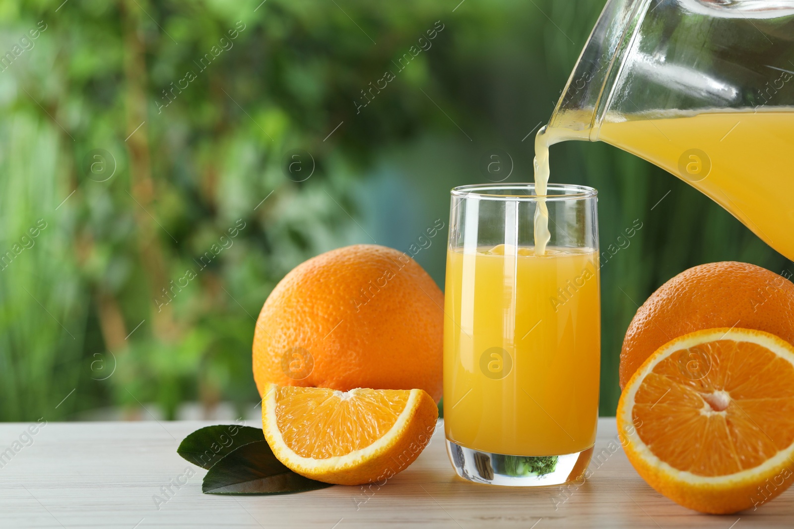 Photo of Pouring tasty orange juice into glass at white wooden table outdoors. Space for text