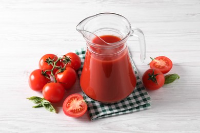 Photo of Tasty tomato juice in glass jug and fresh vegetables on white wooden table