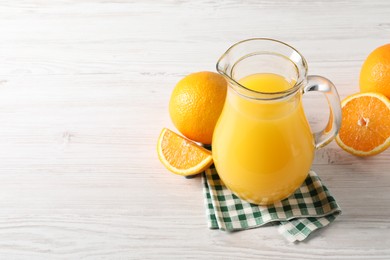 Photo of Tasty orange juice in glass jug and fresh fruits on white wooden table, space for text