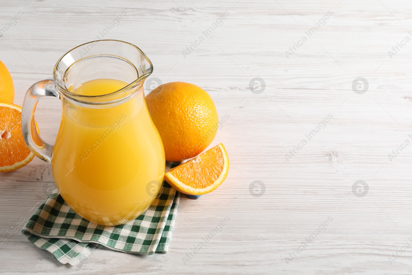 Photo of Tasty orange juice in glass jug and fresh fruits on white wooden table, space for text