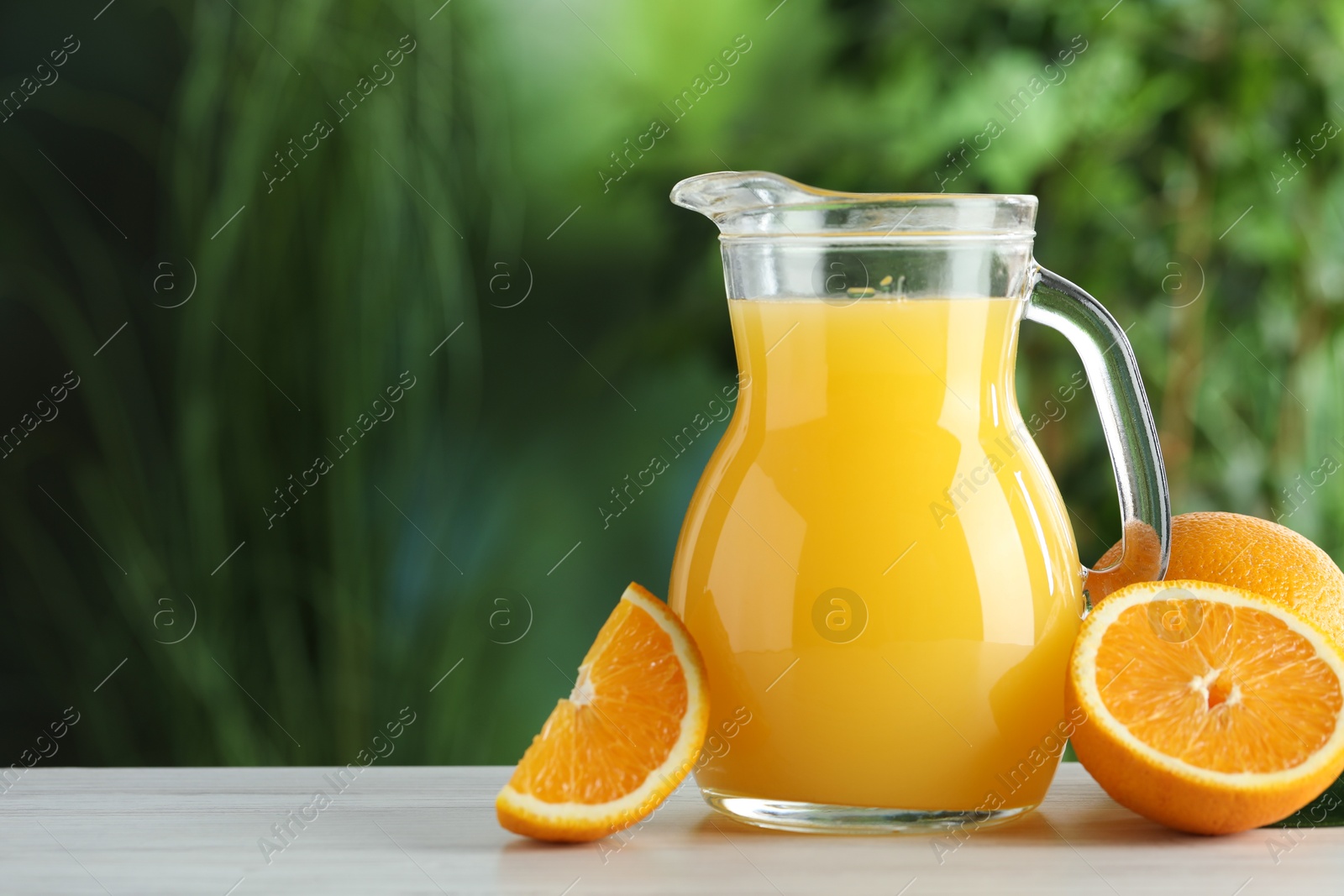 Photo of Tasty orange juice in glass jug and fresh fruits on white wooden table outdoors, space for text