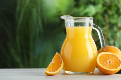 Tasty orange juice in glass jug and fresh fruits on white wooden table outdoors, space for text