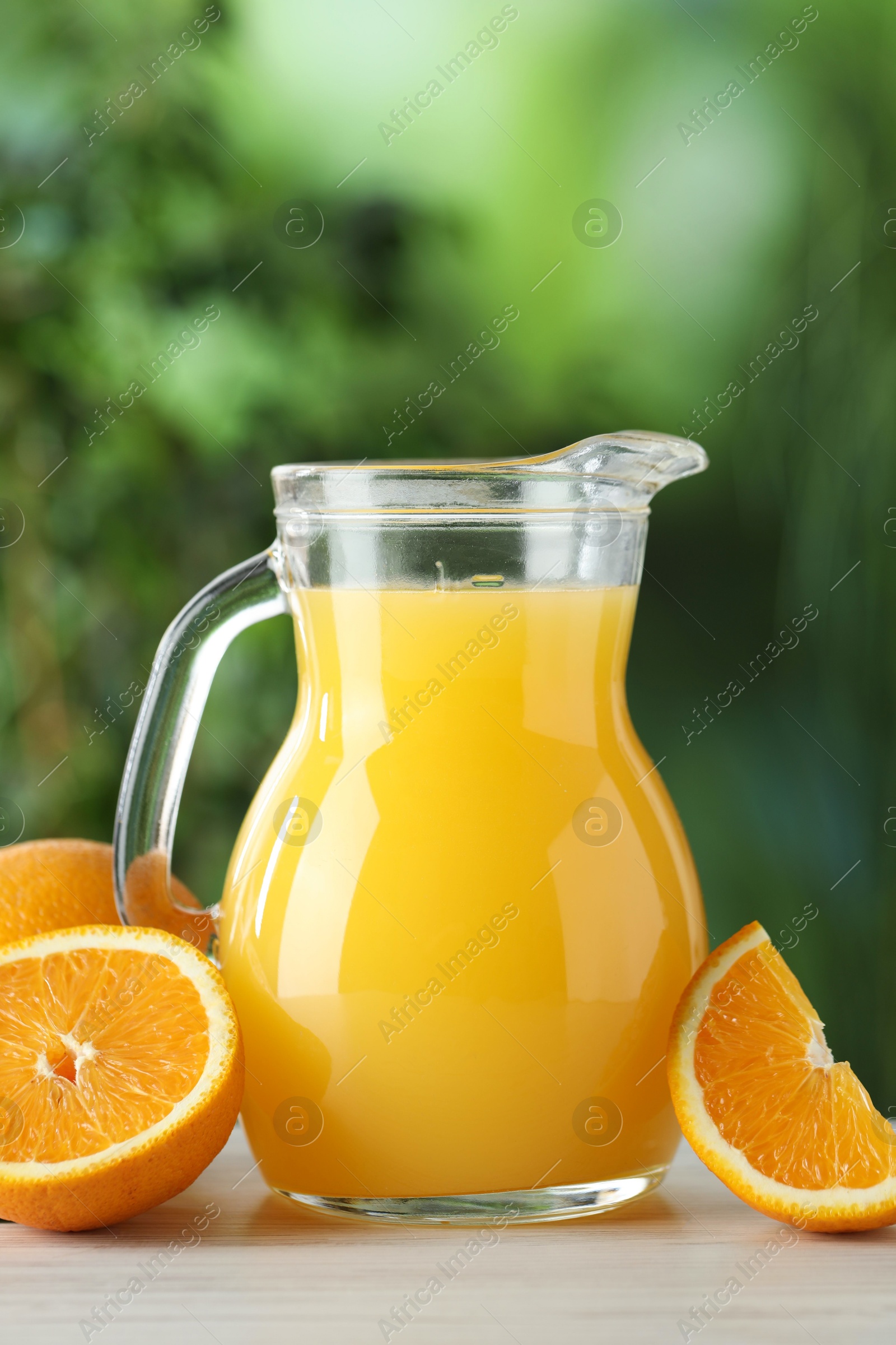 Photo of Tasty orange juice in glass jug and fresh fruits on white wooden table outdoors