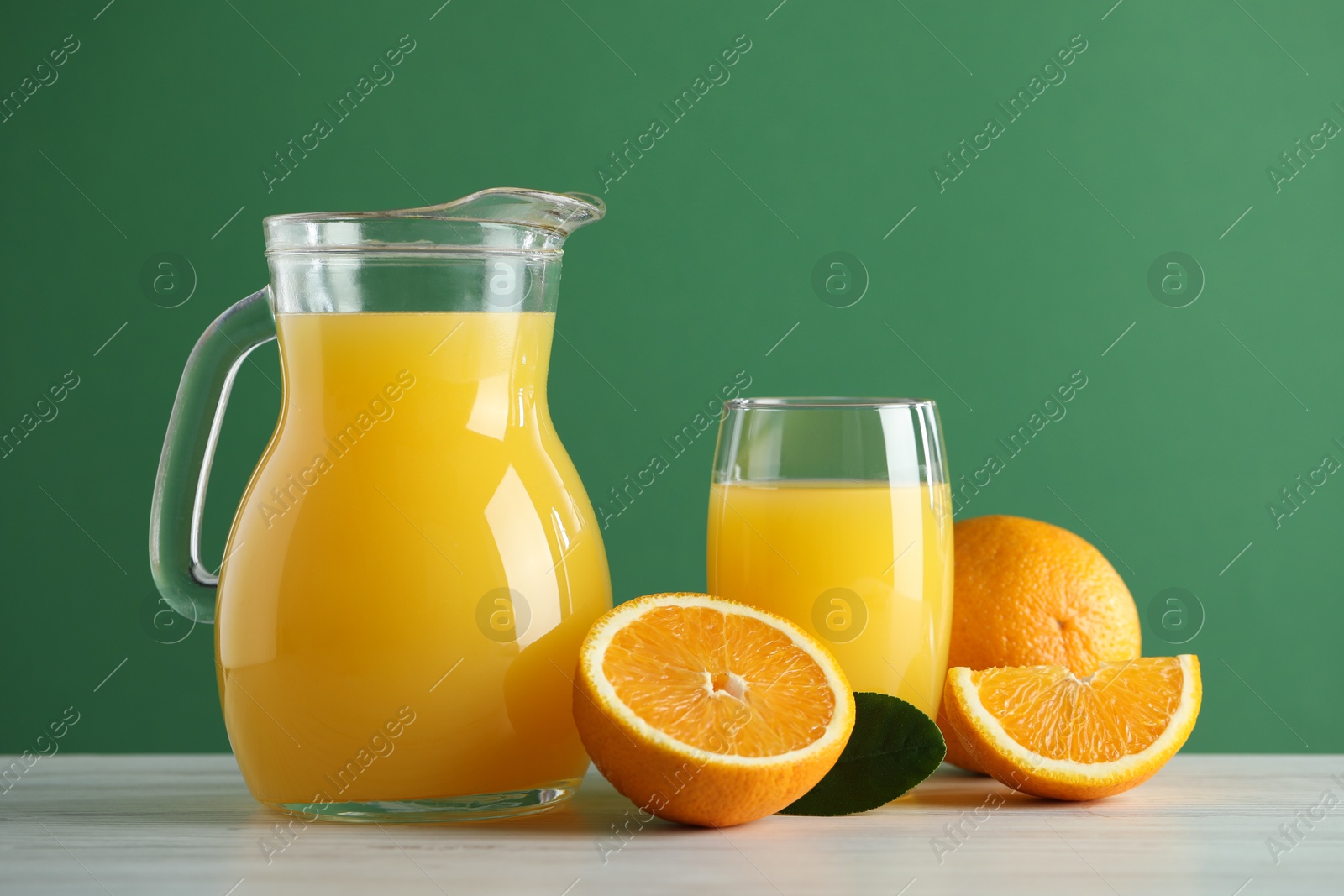 Photo of Tasty orange juice, fresh fruits and green leaf on white wooden table