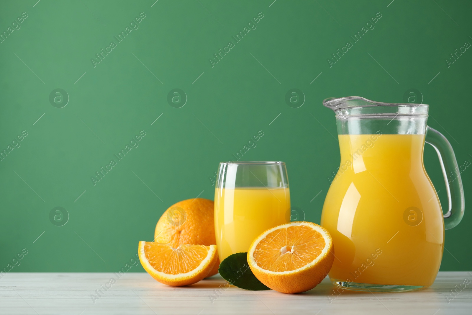 Photo of Tasty orange juice, fresh fruits and green leaf on white wooden table, space for text