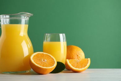 Tasty orange juice, fresh fruits and green leaf on white wooden table, space for text