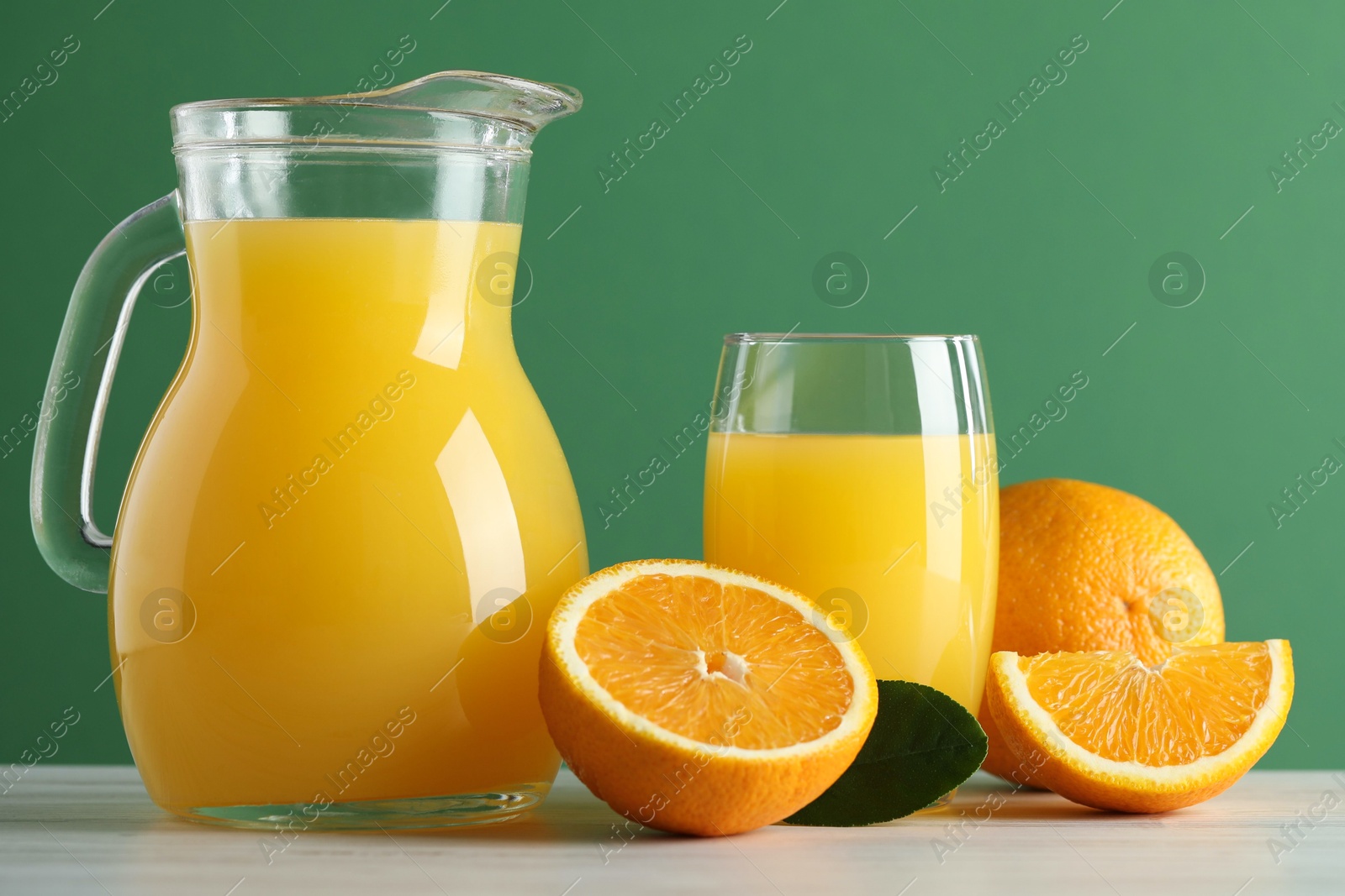 Photo of Tasty orange juice, fresh fruits and green leaf on white wooden table