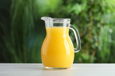 Photo of Fresh orange juice in glass jug on white wooden table outdoors