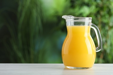 Photo of Fresh orange juice in glass jug on white wooden table outdoors, space for text