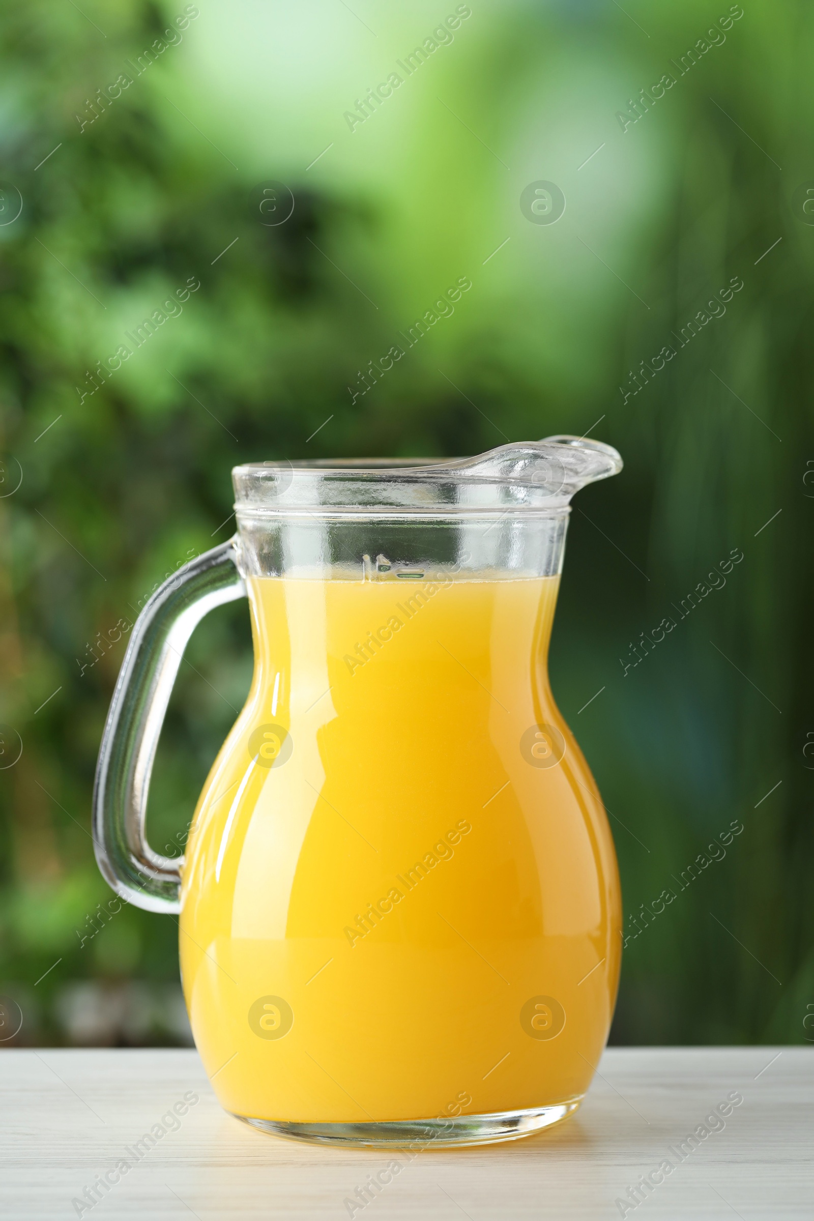 Photo of Fresh orange juice in glass jug on white wooden table outdoors