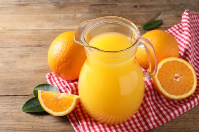 Photo of Tasty orange juice in glass jug, fresh fruits and green leaves on wooden table