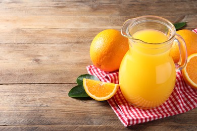 Tasty orange juice in glass jug, fresh fruits and green leaves on wooden table, space for text