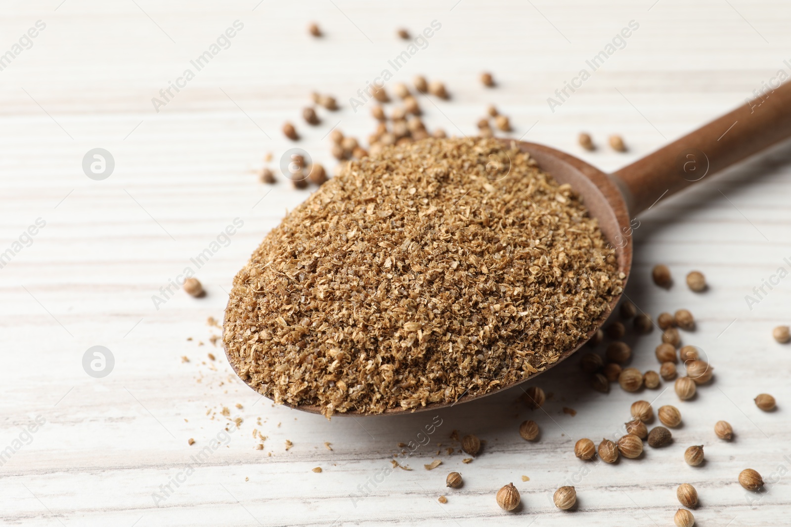 Photo of Coriander powder in spoon and seeds on wooden table, closeup