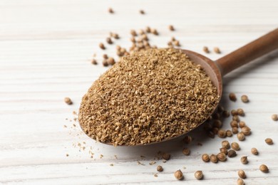 Coriander powder in spoon and seeds on wooden table, closeup