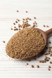 Coriander powder in spoon and seeds on wooden table