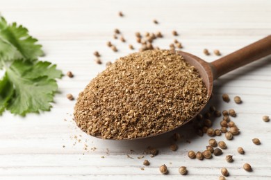 Photo of Coriander powder in spoon, seeds and green leaves on wooden table, closeup