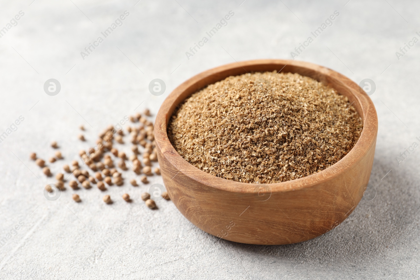 Photo of Coriander powder in bowl and seeds on light grey table