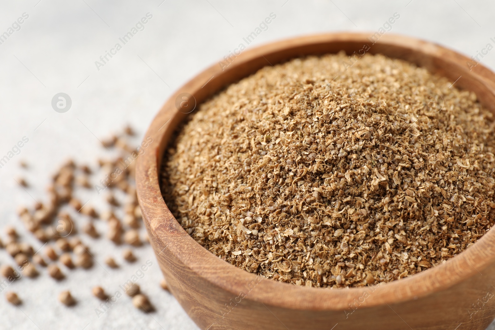 Photo of Coriander powder in bowl and seeds on light grey table, closeup