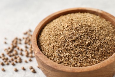 Coriander powder in bowl and seeds on light grey table, closeup