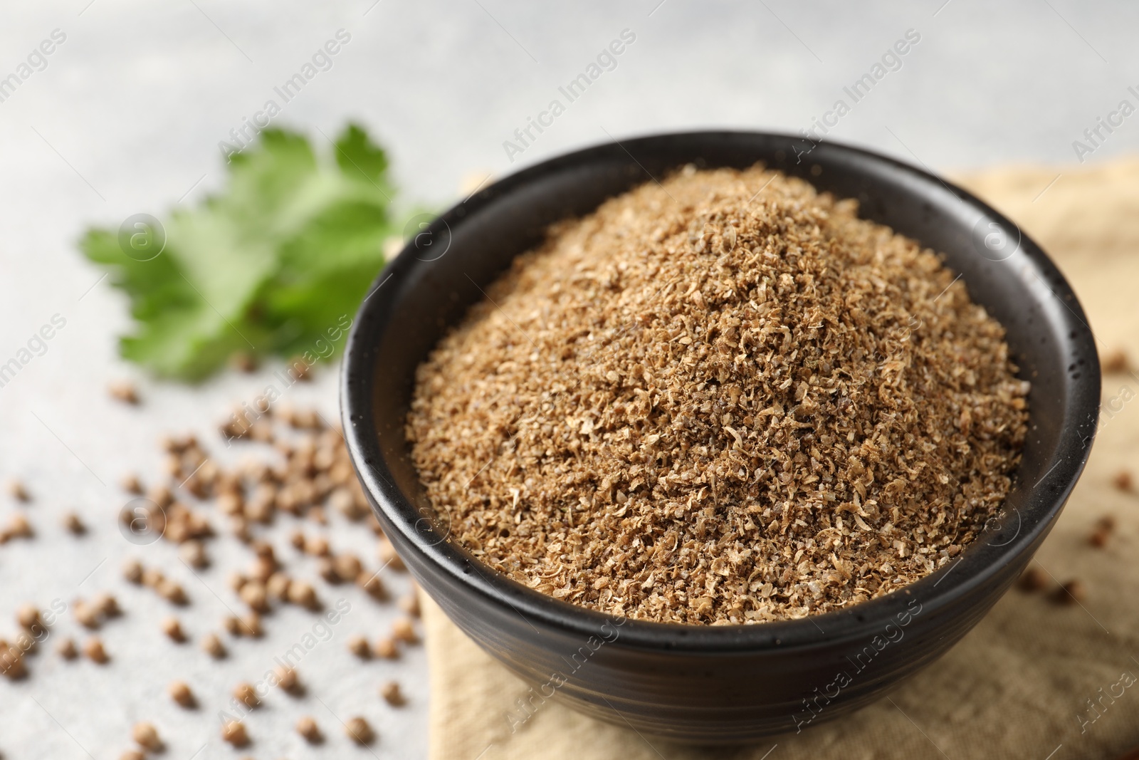 Photo of Coriander powder in bowl and seeds on table, closeup