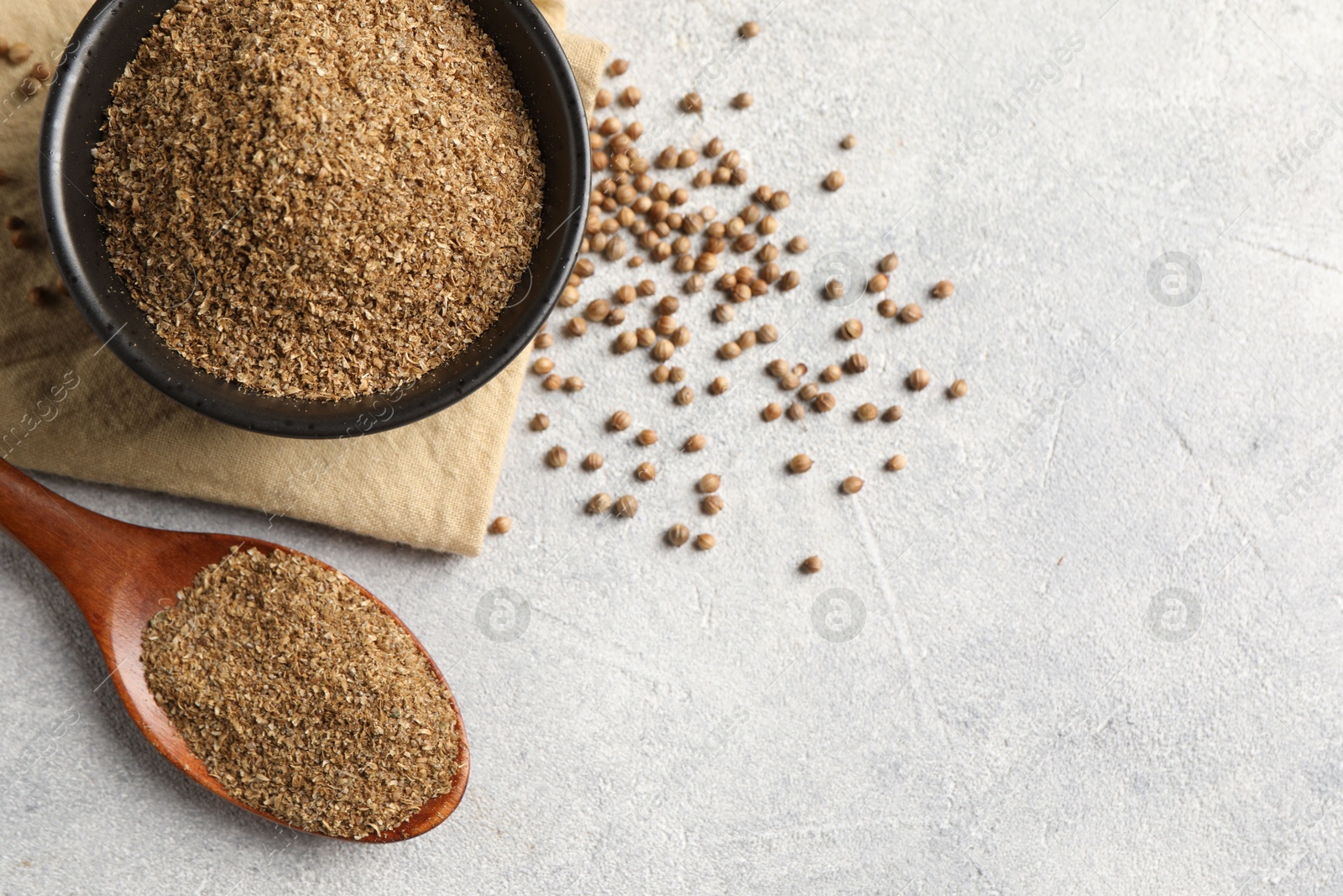 Photo of Coriander powder in bowl, spoon and seeds on light grey table, top view. Space for text