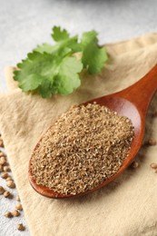 Photo of Coriander powder in spoon, seeds and green leaves on table