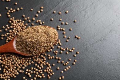 Photo of Coriander powder in spoon and seeds on black table, top view. Space for text
