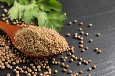 Photo of Coriander powder in spoon, seeds and green leaves on black table, closeup