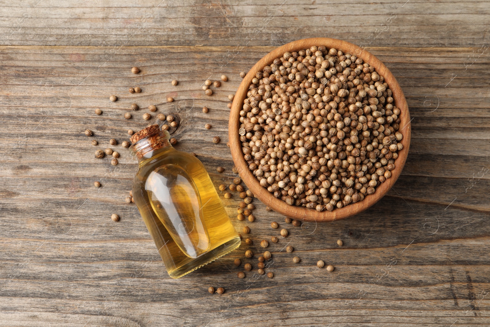 Photo of Coriander essential oil and seeds on wooden table, top view