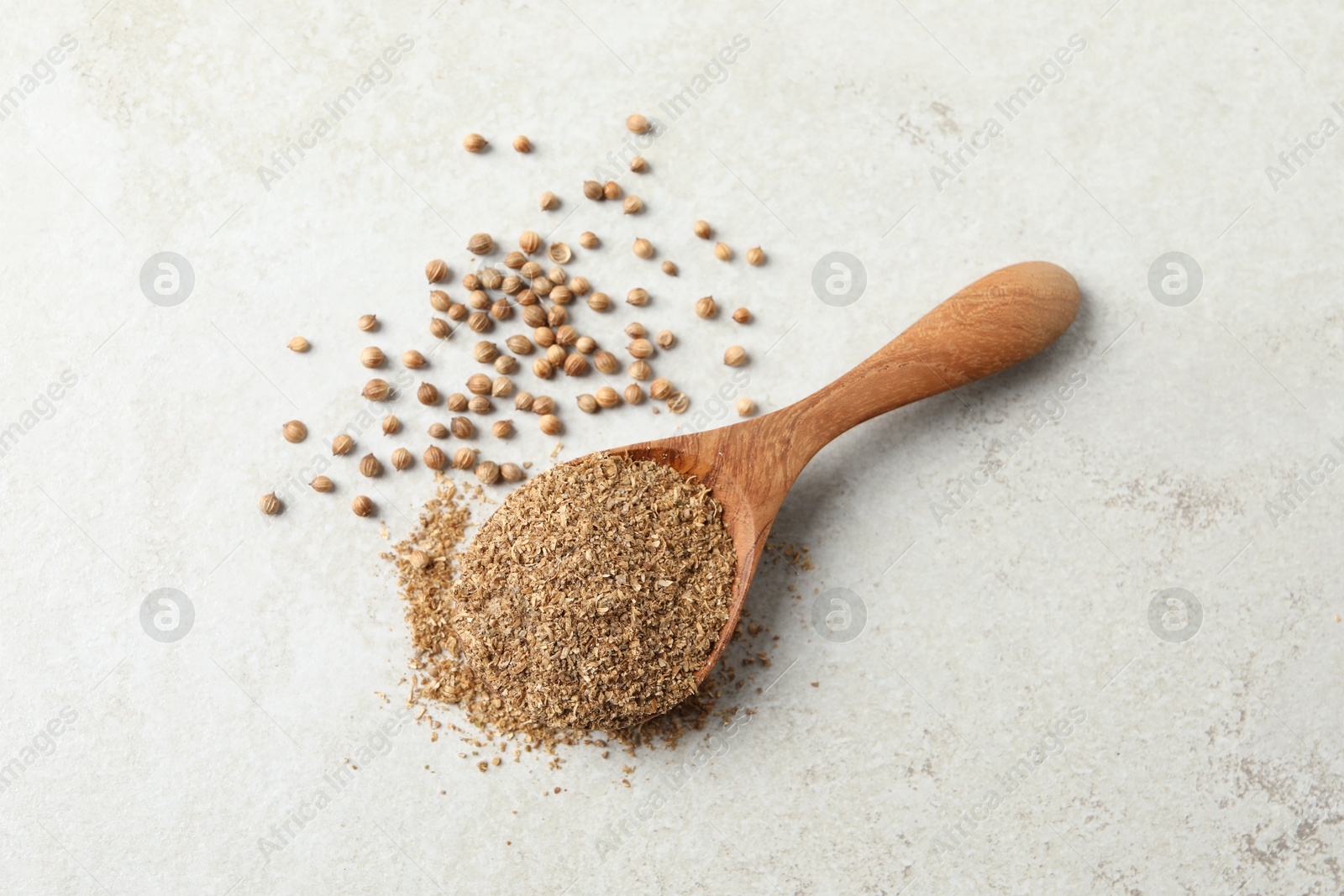 Photo of Coriander powder in spoon and seeds on light grey table, above view