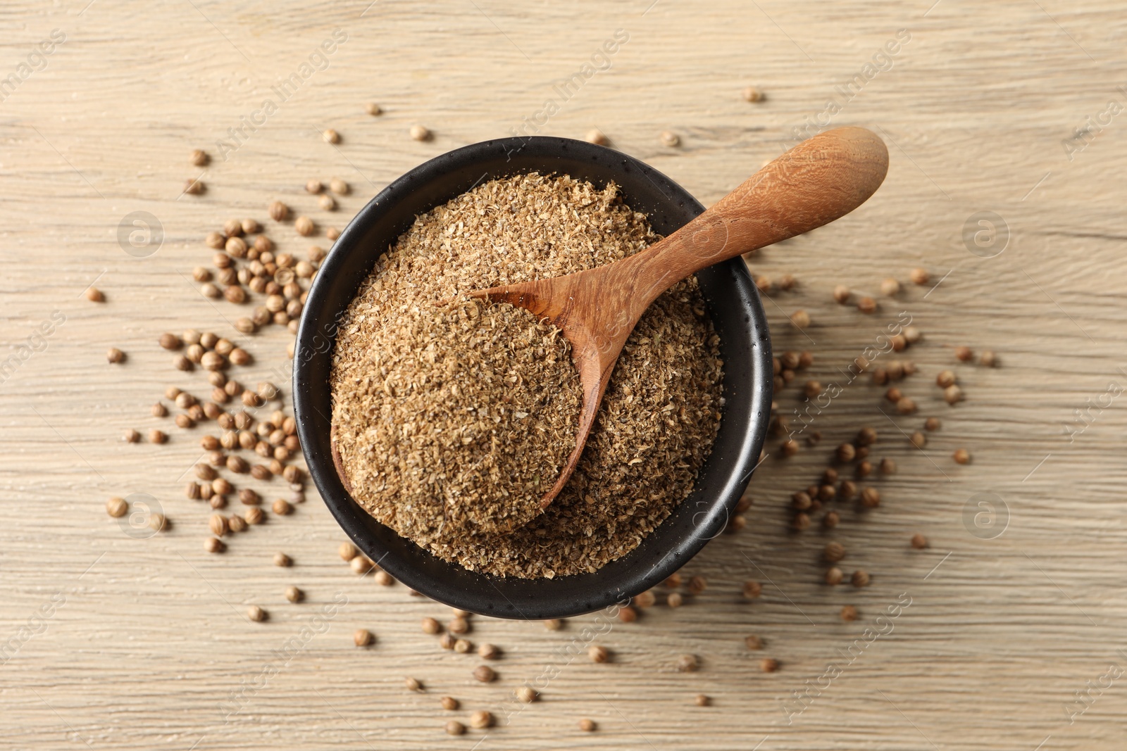 Photo of Coriander powder in bowl, spoon and seeds on wooden table, top view