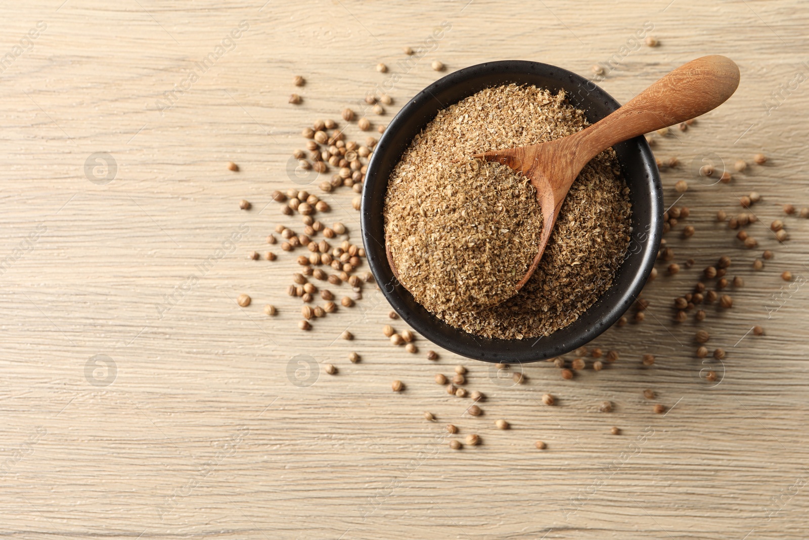Photo of Coriander powder in bowl, spoon and seeds on wooden table, top view. Space for text