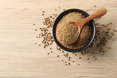 Coriander powder in bowl, spoon and seeds on wooden table, top view. Space for text