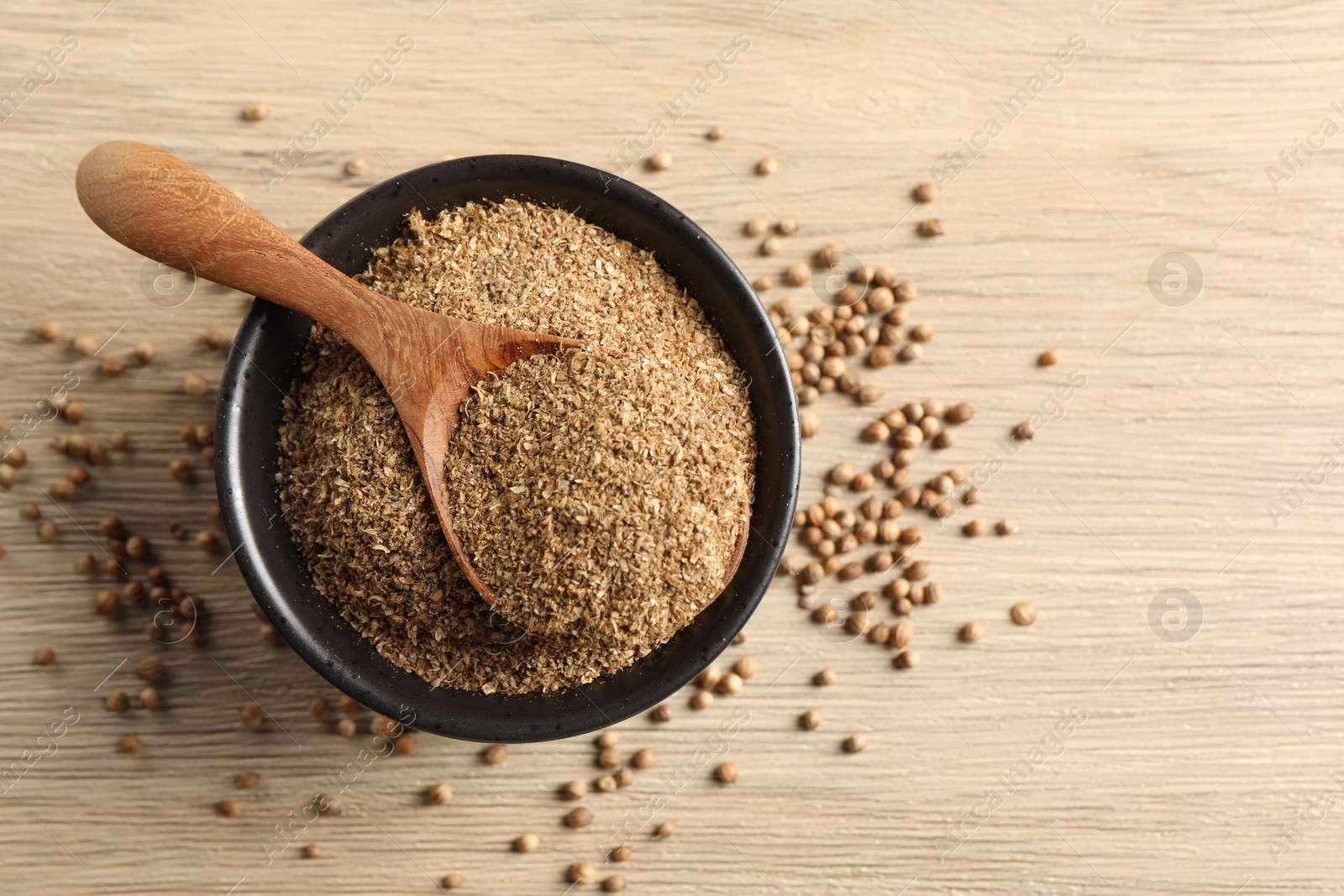 Photo of Coriander powder in bowl, spoon and seeds on wooden table, top view
