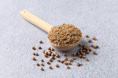 Photo of Coriander powder in spoon and seeds on grey table