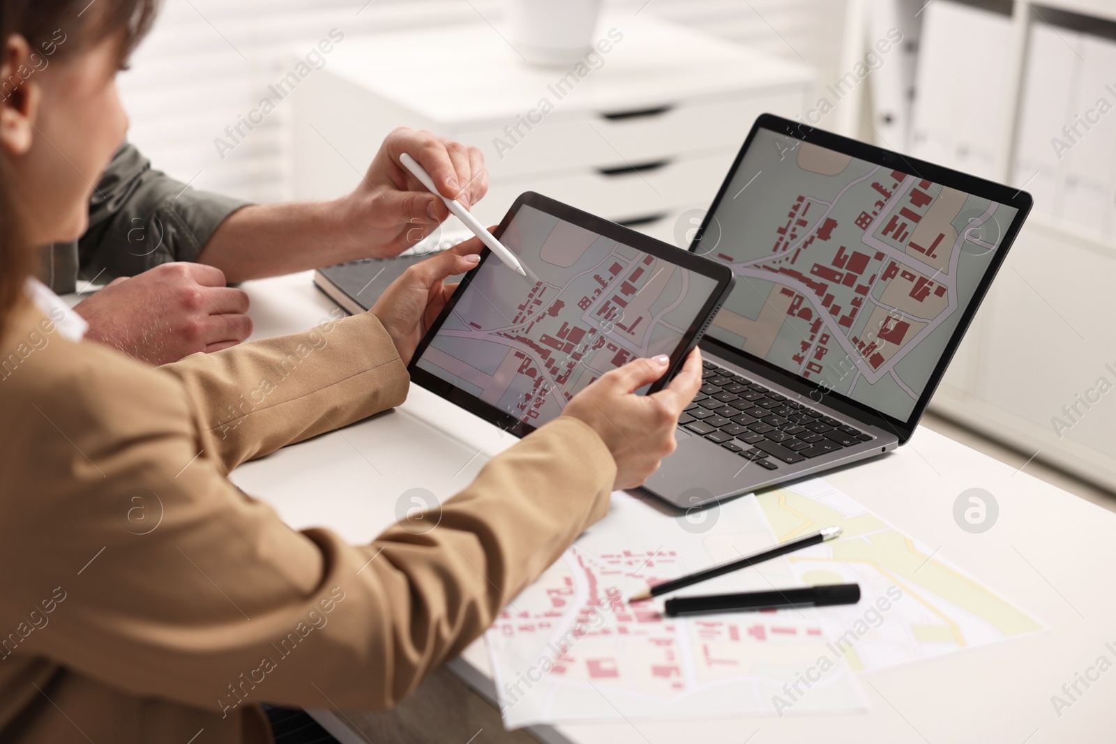 Photo of Cartographers working with cadastral map on tablet at white table in office, closeup