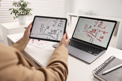 Photo of Cartographer working with cadastral maps on devices at white table in office, closeup