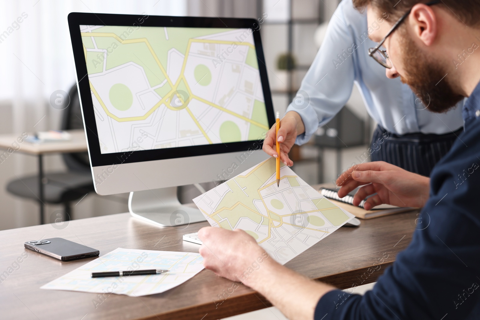 Photo of Cartographers working with cadastral maps at wooden table in office, closeup