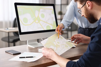 Cartographers working with cadastral maps at wooden table in office, closeup