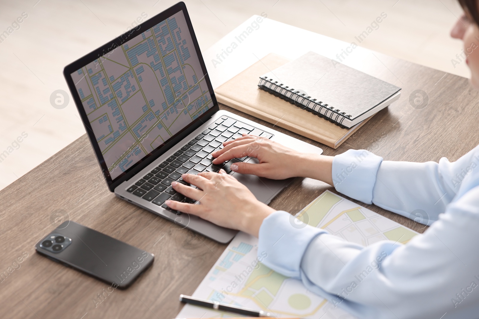 Photo of Cartographer working with cadastral map on laptop at wooden table in office, closeup